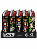 A retail display tray of BIC lighters with black bodies decorated with colorful Day of the Dead style graphics, including skulls, flowers, a skeleton, and cactus motifs. The lighters have red tops and silver metal tips, arranged in rows on a black branded tray.
