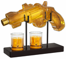 Glass gun-shaped decanter with two glasses on a stand, filled with a yellow liquid.